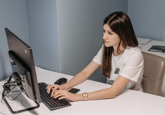 Brunette woman typing on computer in a healthcare office setting, focused on her tasks.